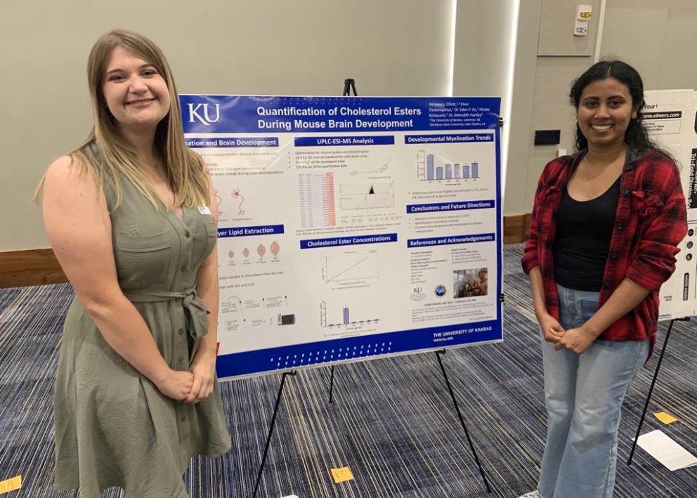 Two group members standing in front of the REU poster