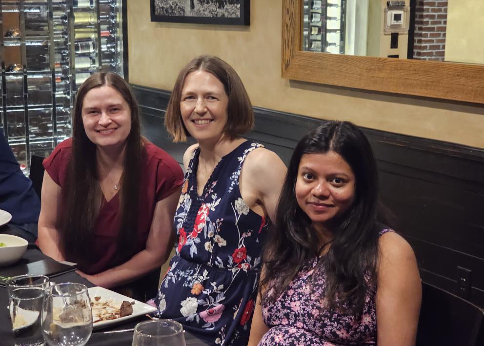 Three women sit at dinner table and pose for photo