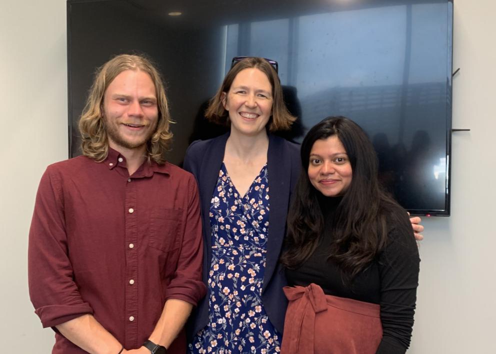 Three people smile in front of TV monitor
