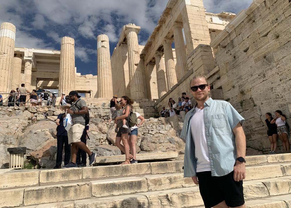 Person stands in front of ancient Greek ruins