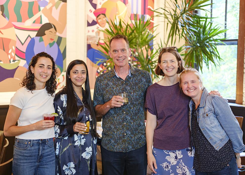 Five people hold drinks and smile at the camera 