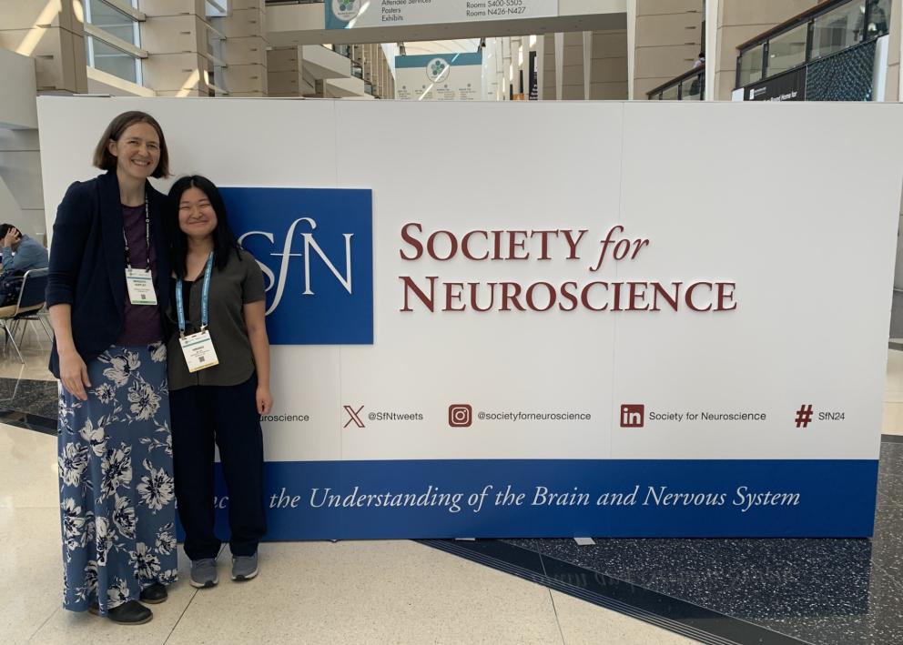 Two people pose in front of Society for Neuroscience large sign