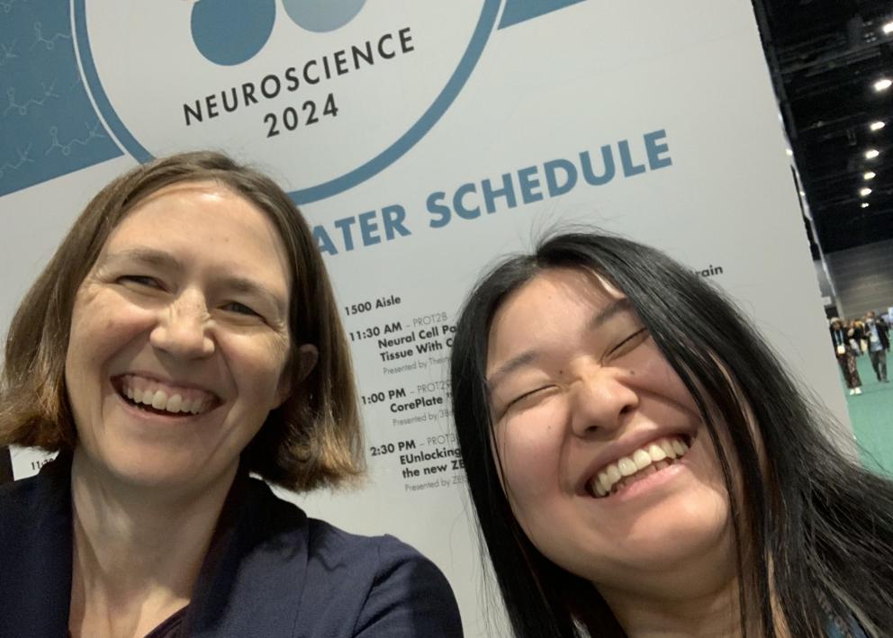 Two people smile in front of a conference poster sign