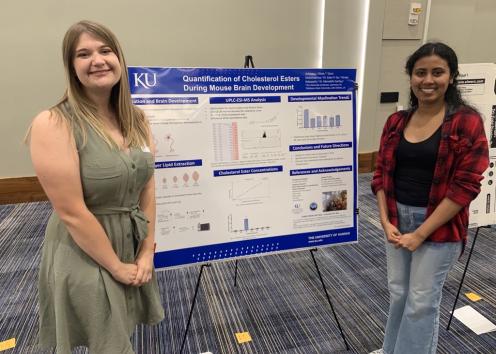 Two group members standing in front of the REU poster
