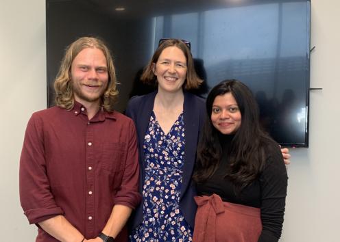 Three people smile in front of TV monitor