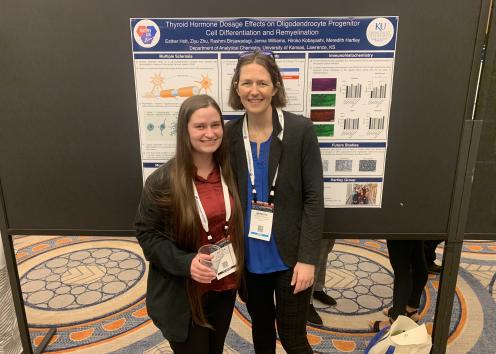 Two people stand in front of a poster.