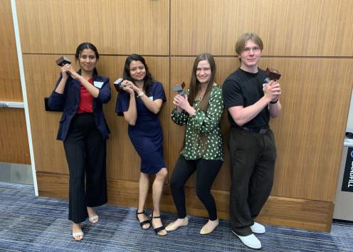 Four students pose like Charlie's Angels holding statues