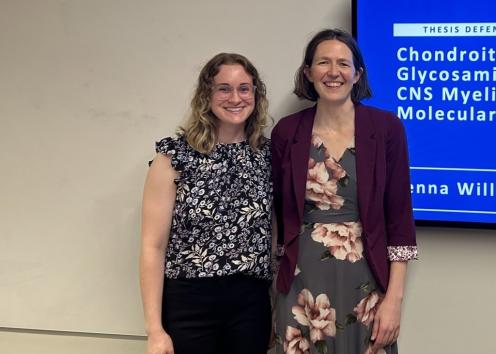 Two women stand by a display screen