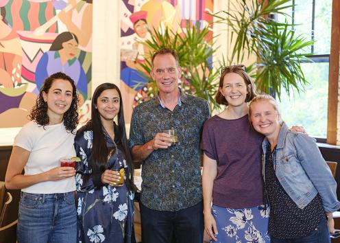 Five people hold drinks and smile at the camera 
