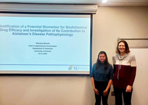 Two women stand next to a projected scientific presentation